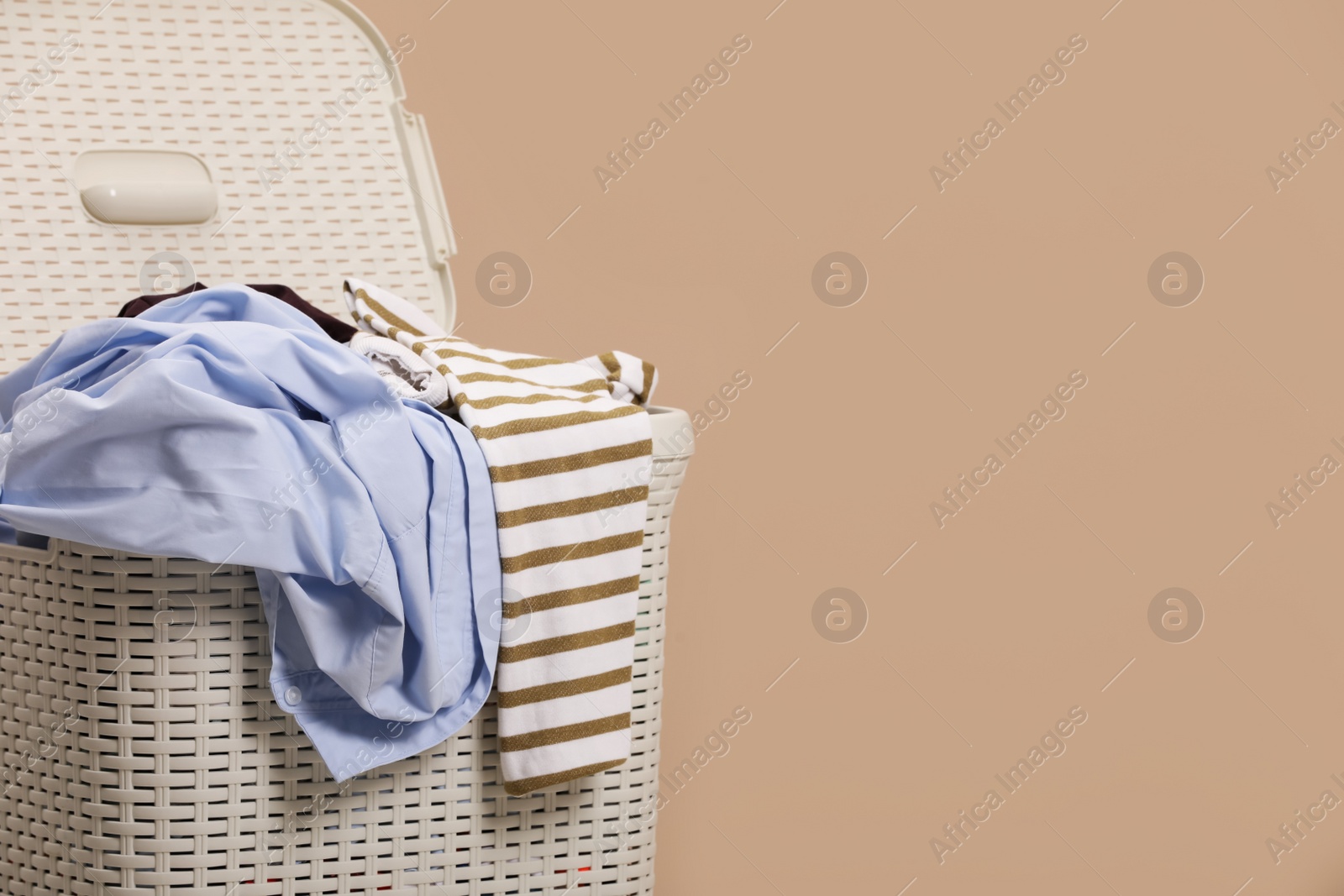Photo of Plastic laundry basket with clothes near beige wall. Space for text