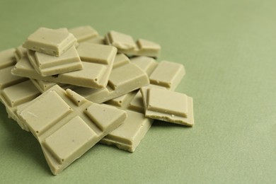 Photo of Pieces of tasty matcha chocolate bars on green background, closeup. Space for text