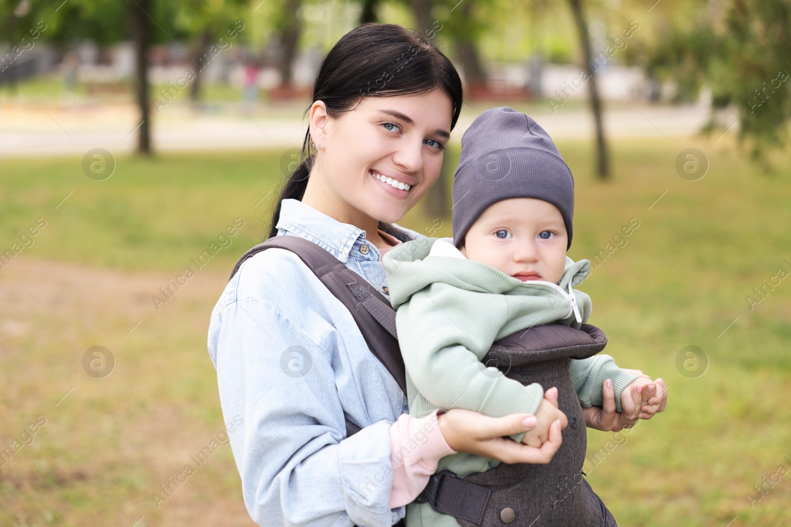 Photo of Mother holding her child in sling (baby carrier) in park