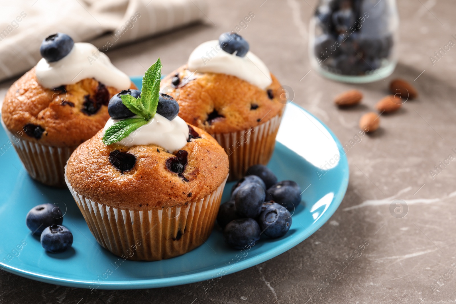 Photo of Plate of tasty muffins and blueberries on marble table