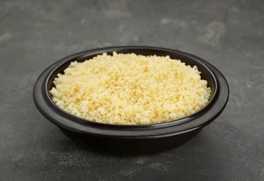 Photo of Bowl of tasty couscous on grey table, closeup