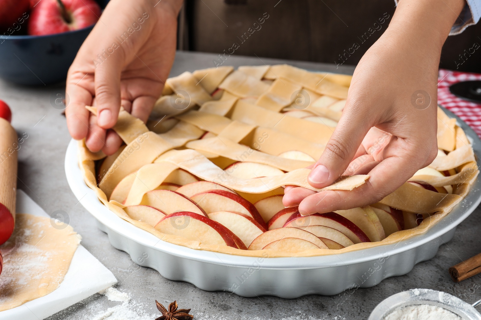 Photo of Woman decorating raw apple pie at grey table, closeup