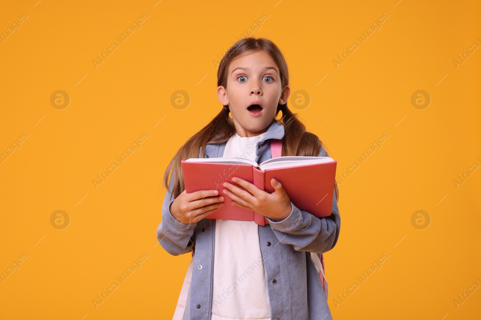 Photo of Emotional schoolgirl with open book on orange background