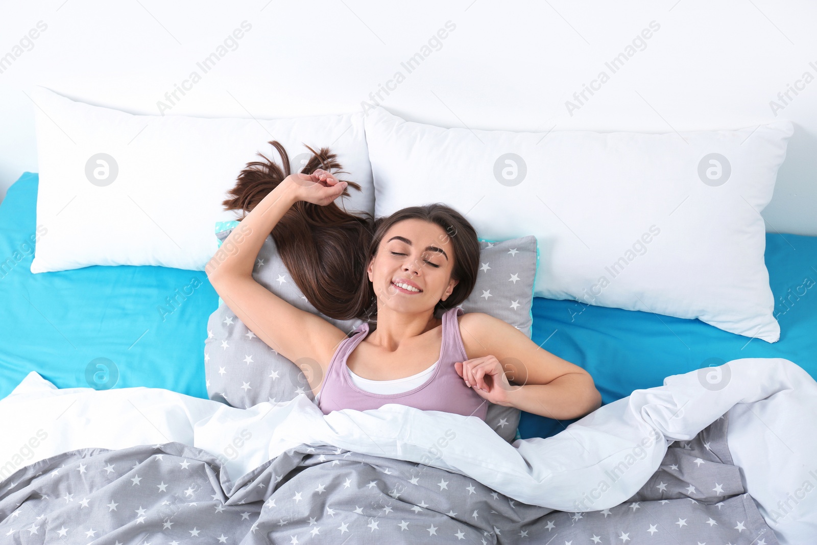 Photo of Young woman stretching under blanket in morning, above view. Bedtime