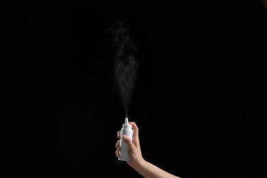 Photo of Nasal congestion. Woman spraying remedy from bottle on black background, closeup