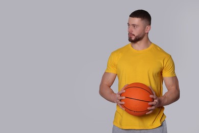 Photo of Athletic young man with basketball ball on light grey background. Space for text