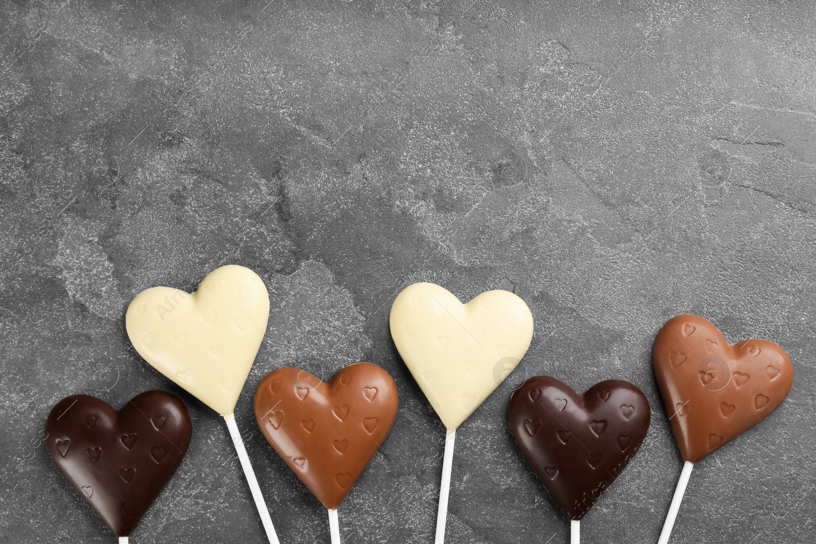 Photo of Different chocolate heart shaped lollipops on grey table, flat lay. Space for text