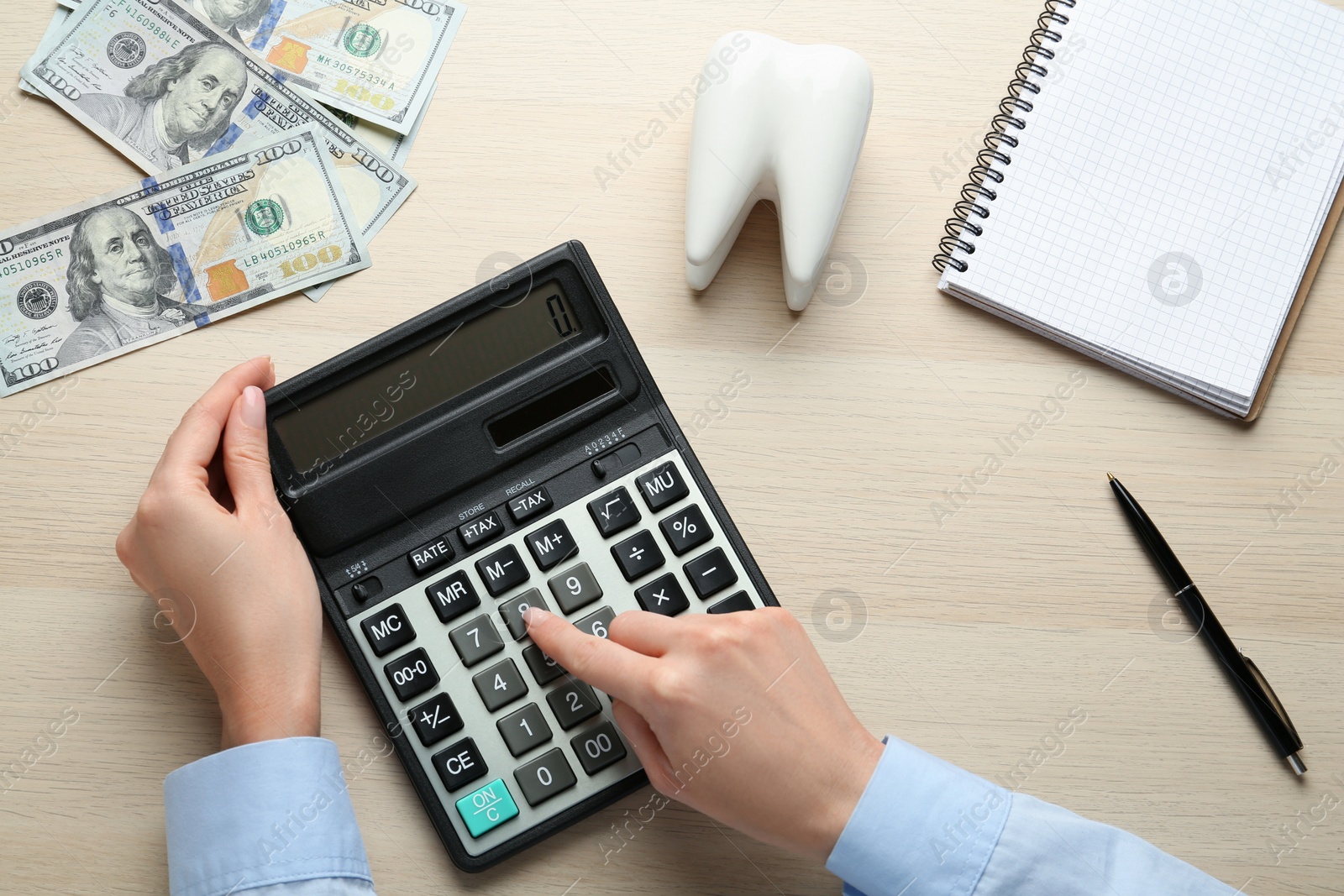 Photo of Ceramic model of tooth and woman counting money with calculator at wooden table, top view. Expensive treatment