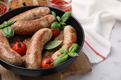 Photo of Bowl with tasty homemade sausages, basil leaves and tomatoes on white table, closeup