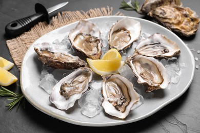 Photo of Delicious fresh oysters with lemon slices served on black slate table, closeup