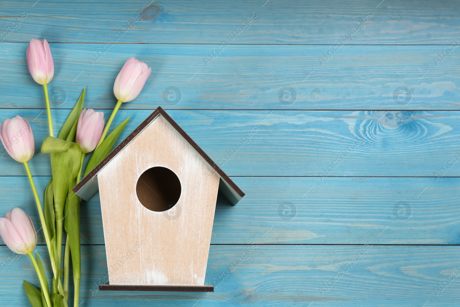 Photo of Beautiful bird house and pink tulips on light blue wooden background, flat lay. Spring composition with space for text