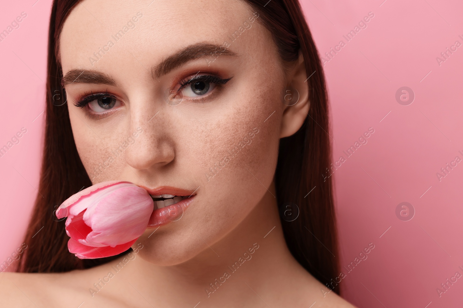 Photo of Beautiful woman with freckles and tulip on pink background, closeup