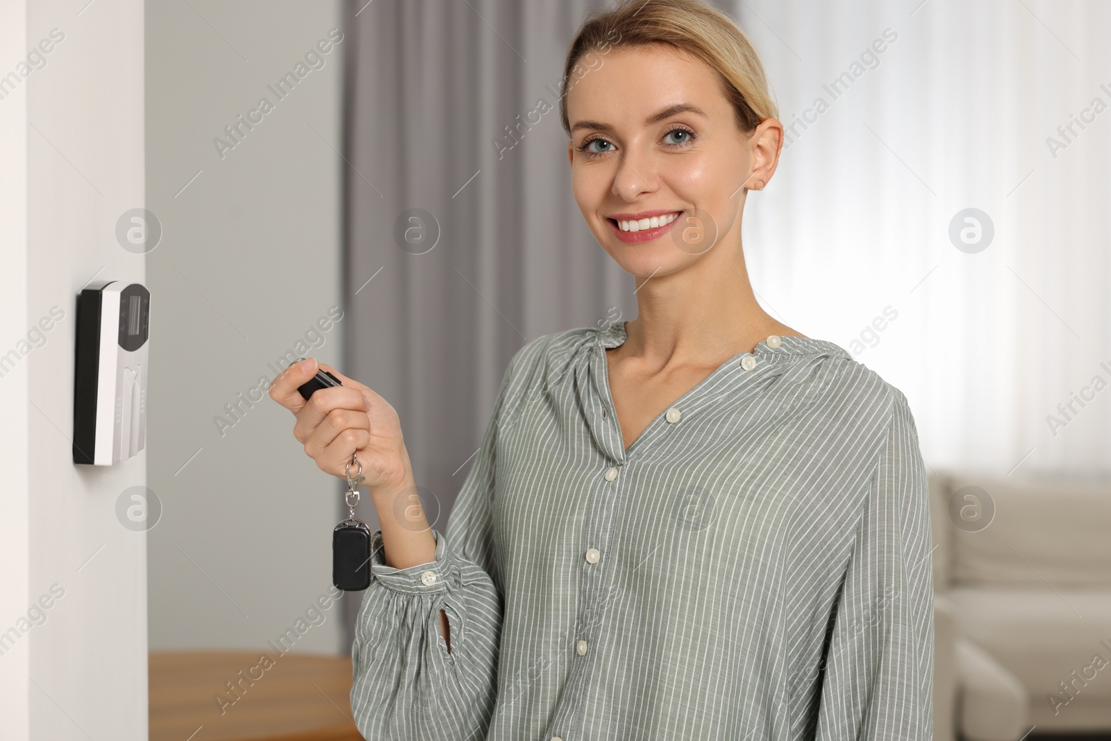 Photo of Home security system. Smiling woman using alarm key fob in room