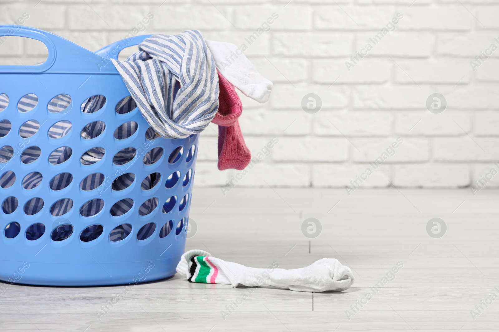 Photo of Laundry basket with clothes near white brick wall. Space for text