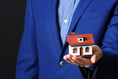 Photo of Male agent holding house model on black background, closeup. Home insurance