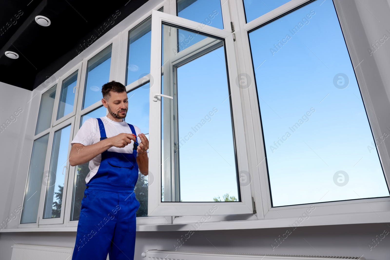 Photo of Construction worker adjusting installed window with screwdriver indoors