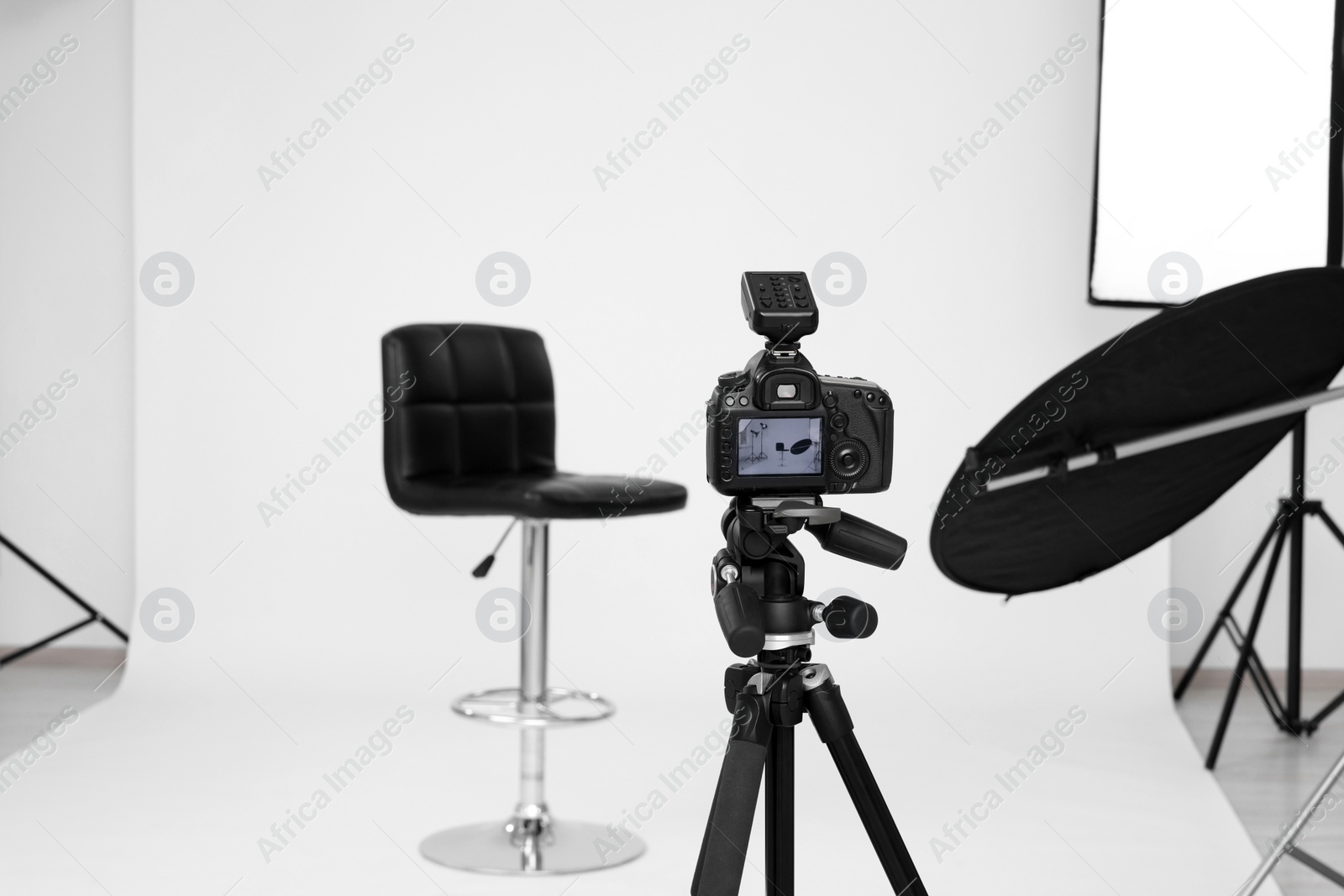 Photo of Camera on tripod, bar stool and professional lighting equipment in modern photo studio, space for text