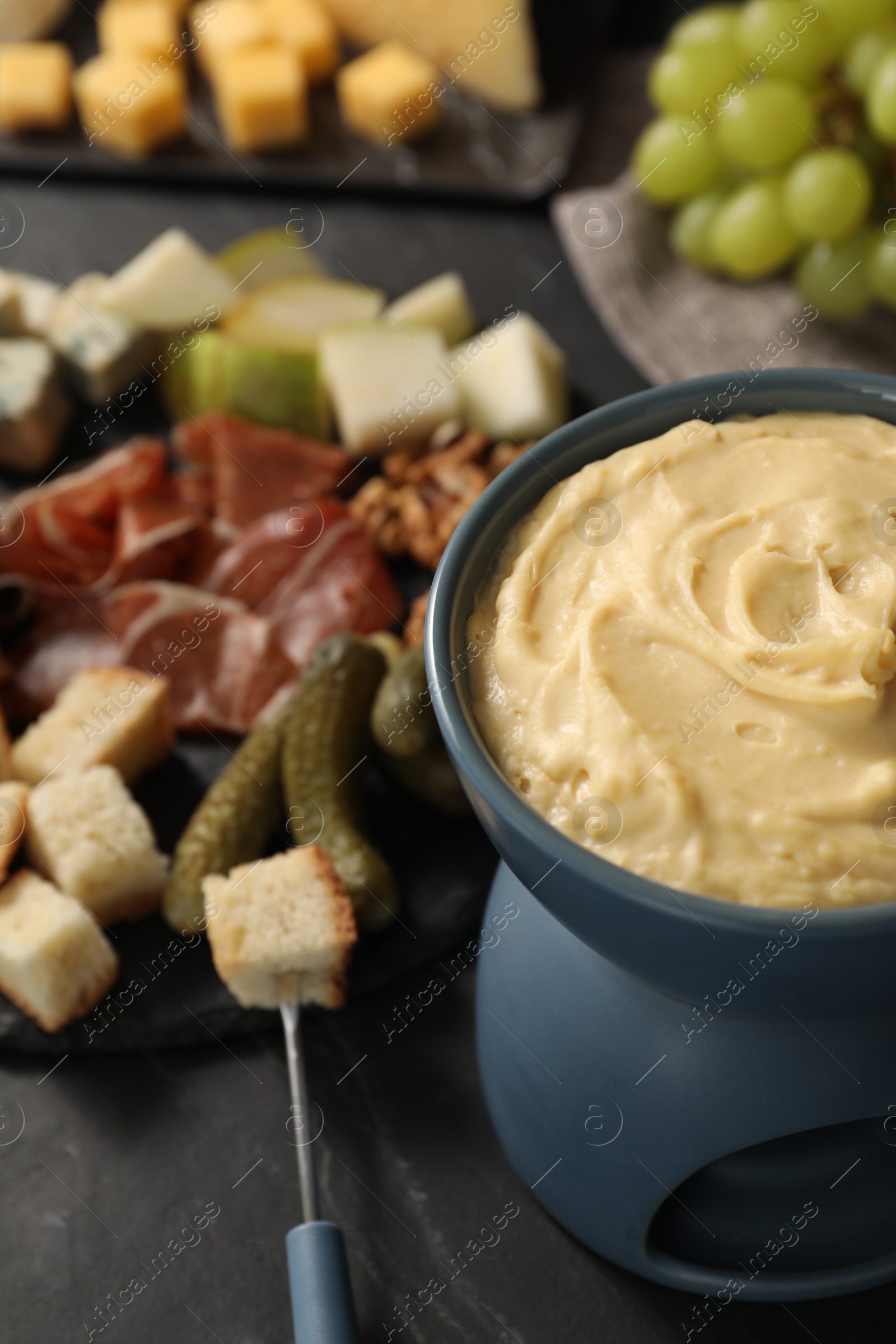 Photo of Fondue with tasty melted cheese, fork and different snacks on black table