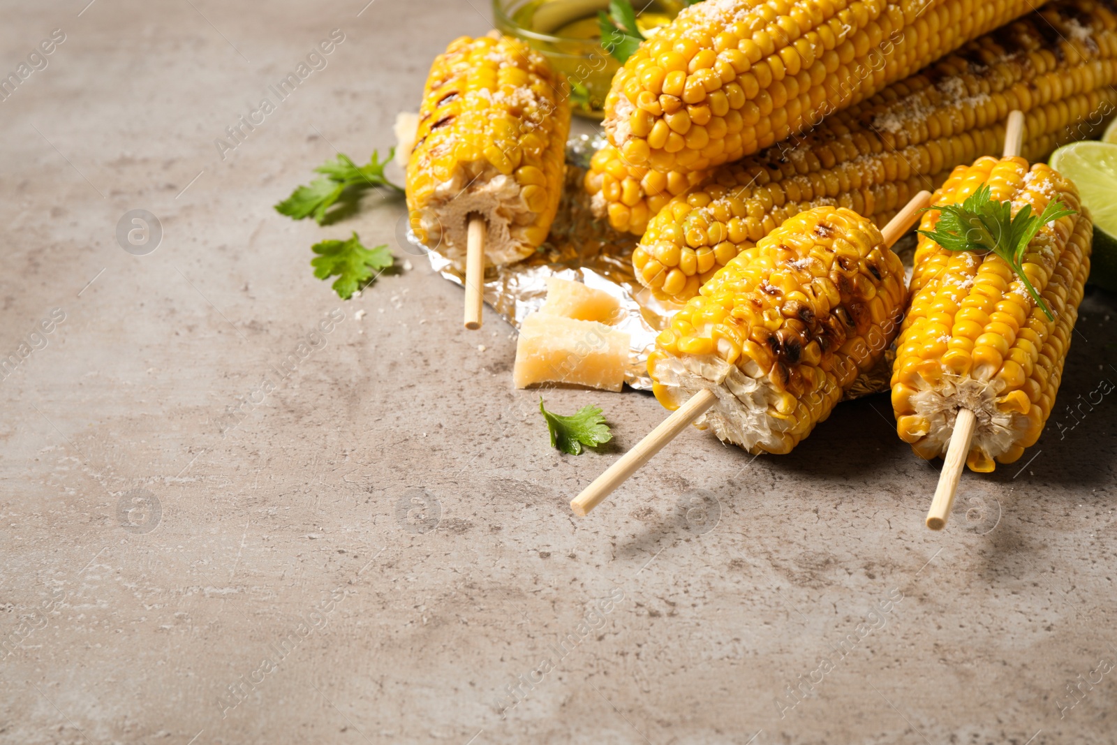 Photo of Delicious grilled corn cobs on grey table. Space for text