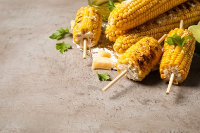 Delicious grilled corn cobs on grey table. Space for text