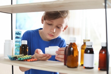 Photo of Little child taking pills from shelf at home. Danger of medicament intoxication