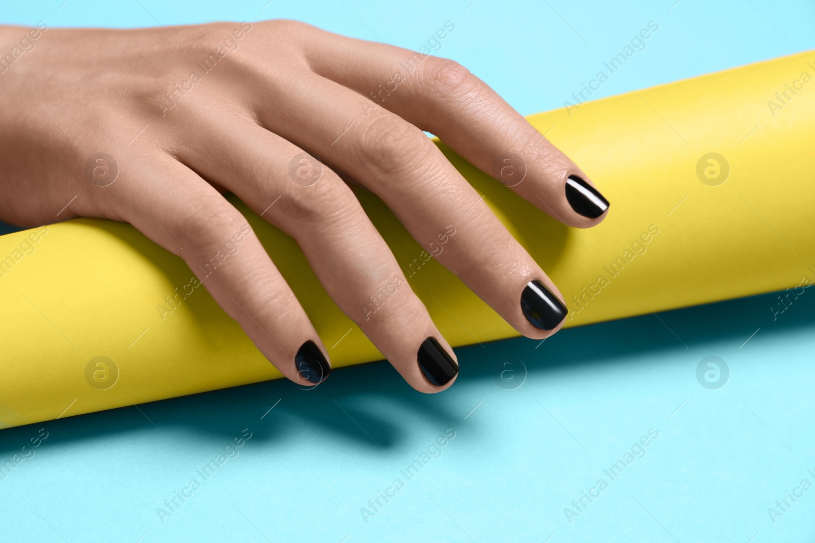 Photo of Woman with black manicure holding paper roll on color background, closeup. Nail polish trends