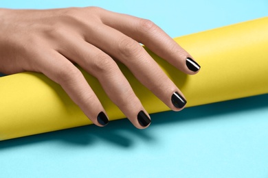 Woman with black manicure holding paper roll on color background, closeup. Nail polish trends