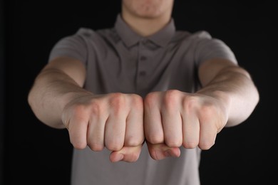 Photo of Man showing fists with space for tattoo on black background, selective focus
