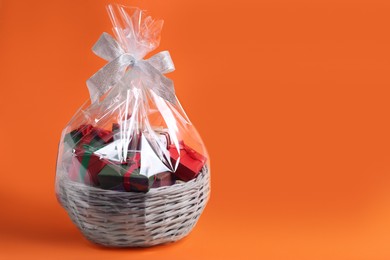 Photo of Wicker basket full of gift boxes on orange background. Space for text