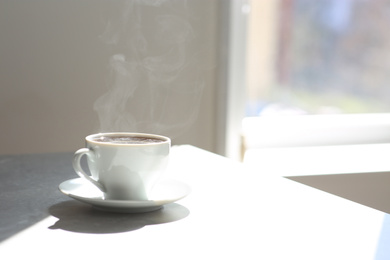 Photo of Cup of delicious coffee on sunlit table, space for text. Good morning