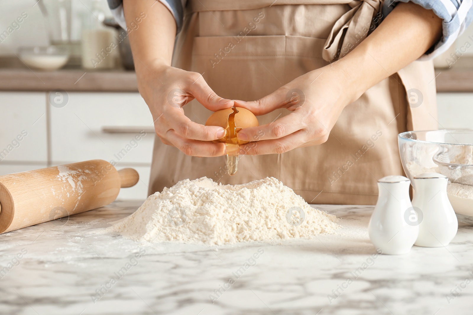 Photo of Woman breaking egg over pile of flour on table in kitchen