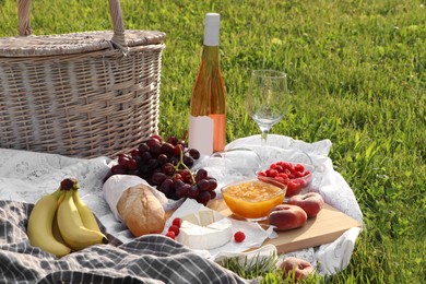 Photo of Picnic blanket with tasty food, basket and cider on green grass outdoors