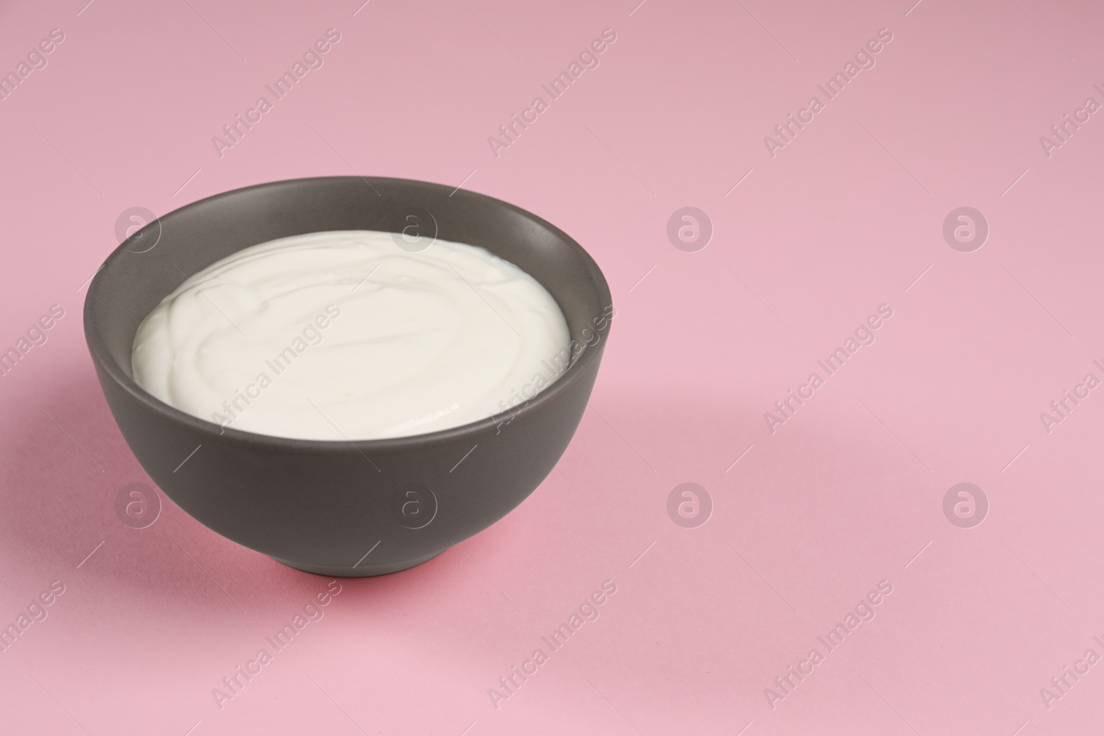 Photo of Bowl of tasty yogurt on pink background, space for text