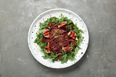 Photo of Plate of tasty bresaola salad with figs, sun-dried tomatoes and balsamic vinegar on grey table, top view