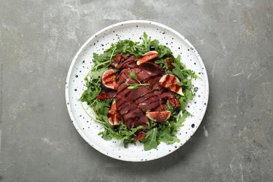 Plate of tasty bresaola salad with figs, sun-dried tomatoes and balsamic vinegar on grey table, top view