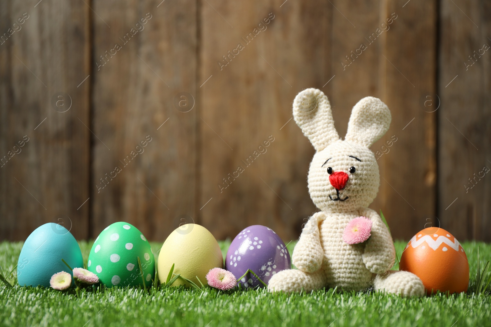 Photo of Colorful Easter eggs and bunny toy on green grass against wooden background