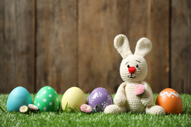 Photo of Colorful Easter eggs and bunny toy on green grass against wooden background