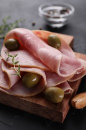 Photo of Tasty ham with olives, garlic and thyme on black table, closeup