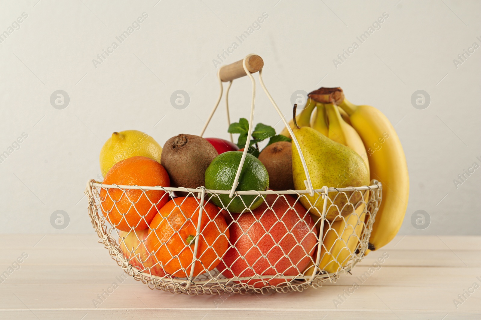 Photo of Fresh ripe fruits in metal basket on white wooden table