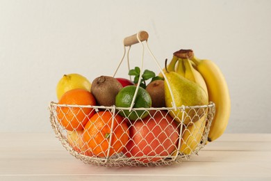 Photo of Fresh ripe fruits in metal basket on white wooden table