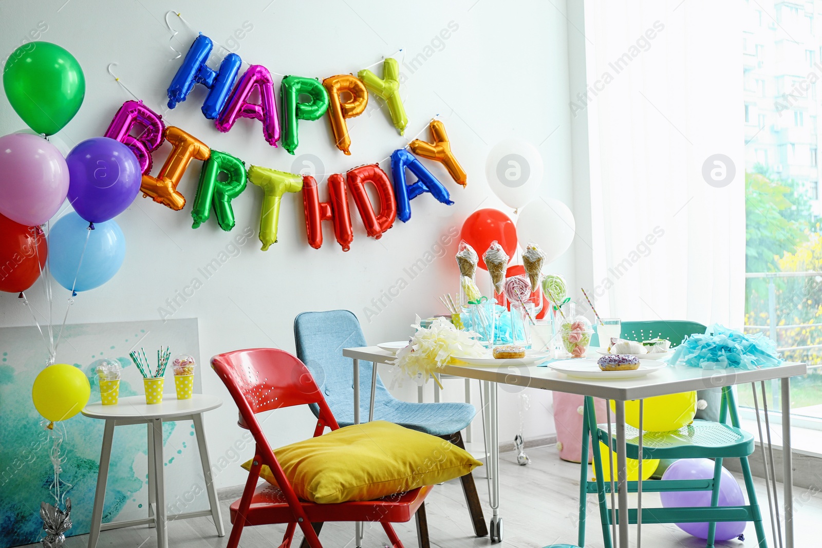 Photo of Table with treats and phrase HAPPY BIRTHDAY made of colorful balloon letters in living room