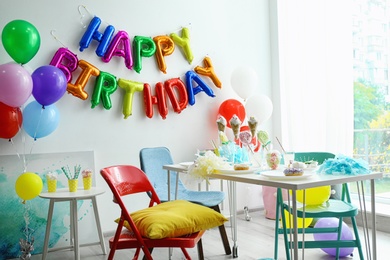 Photo of Table with treats and phrase HAPPY BIRTHDAY made of colorful balloon letters in living room