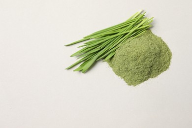 Pile of wheat grass powder and fresh green sprouts on light table, flat lay. Space for text