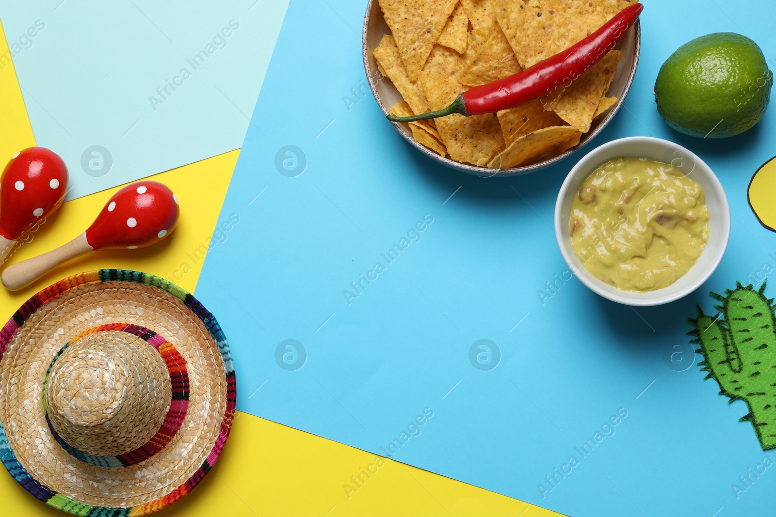 Photo of Mexican sombrero hat, maracas, guacamole, nachos chips, chili and paper cactus on color background, flat lay. Space for text