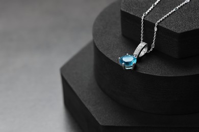 Beautiful necklace with light blue gemstone on black podiums, space for text. Luxury jewelry