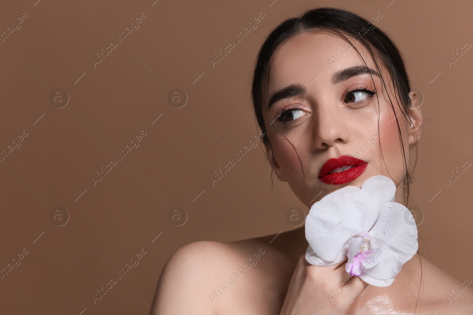 Photo of Portrait of beautiful woman with orchid flower on brown background. Space for text