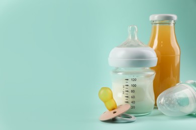 Photo of Milk, juice, pacifier and nibbler on light blue background, space for text. Baby nutrition