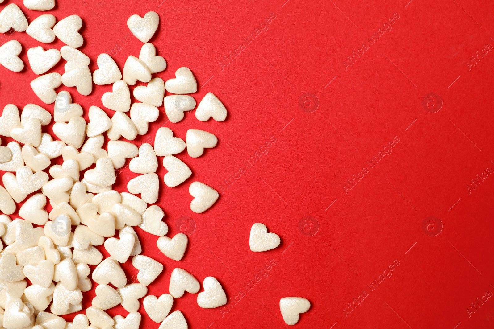 Photo of White heart shaped sprinkles on red background, flat lay. Space for text
