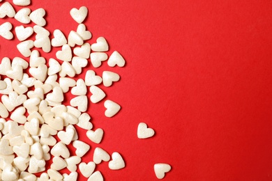 White heart shaped sprinkles on red background, flat lay. Space for text