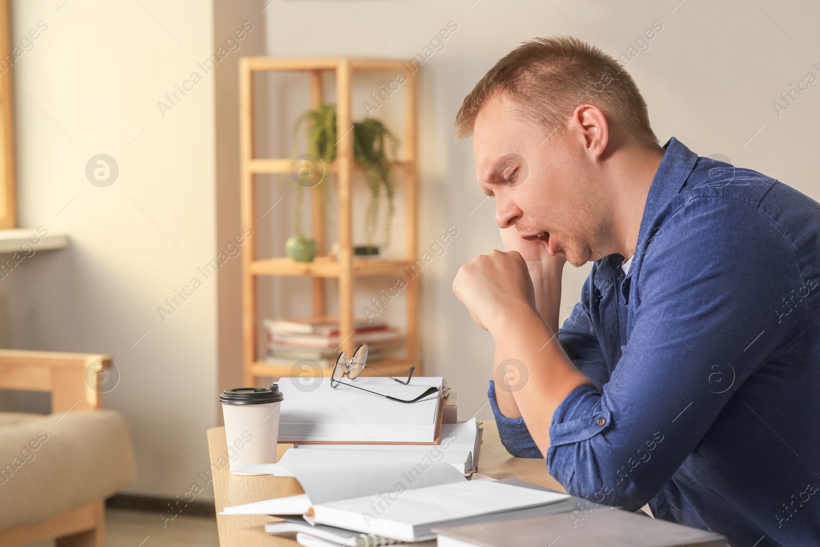 Photo of Tired man studying at wooden table indoors